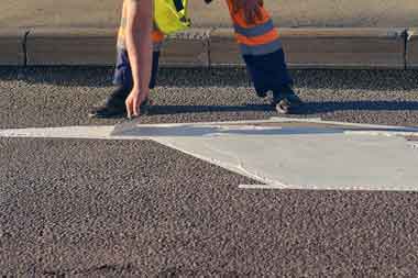 Man troweling paint on commercially paved parking lot lane