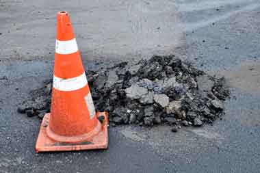 Pothole filled with broken gravel and road cone ready for blacktop repair
