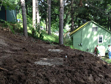 A newly buried septic tank on a hill next to a green house