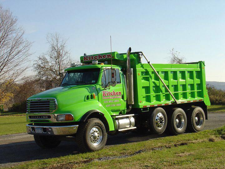 Green dump truck parked on road next to grass