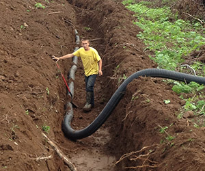 Man in dirt trench with black drainage pipe being installed