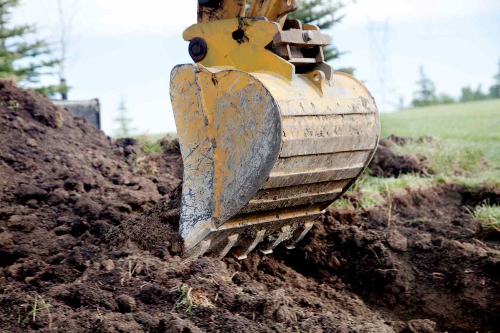 Scoop of an excavator digging in a field of grass and dirt