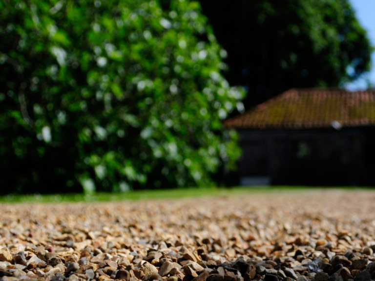Gravel driveway with house and tree in background